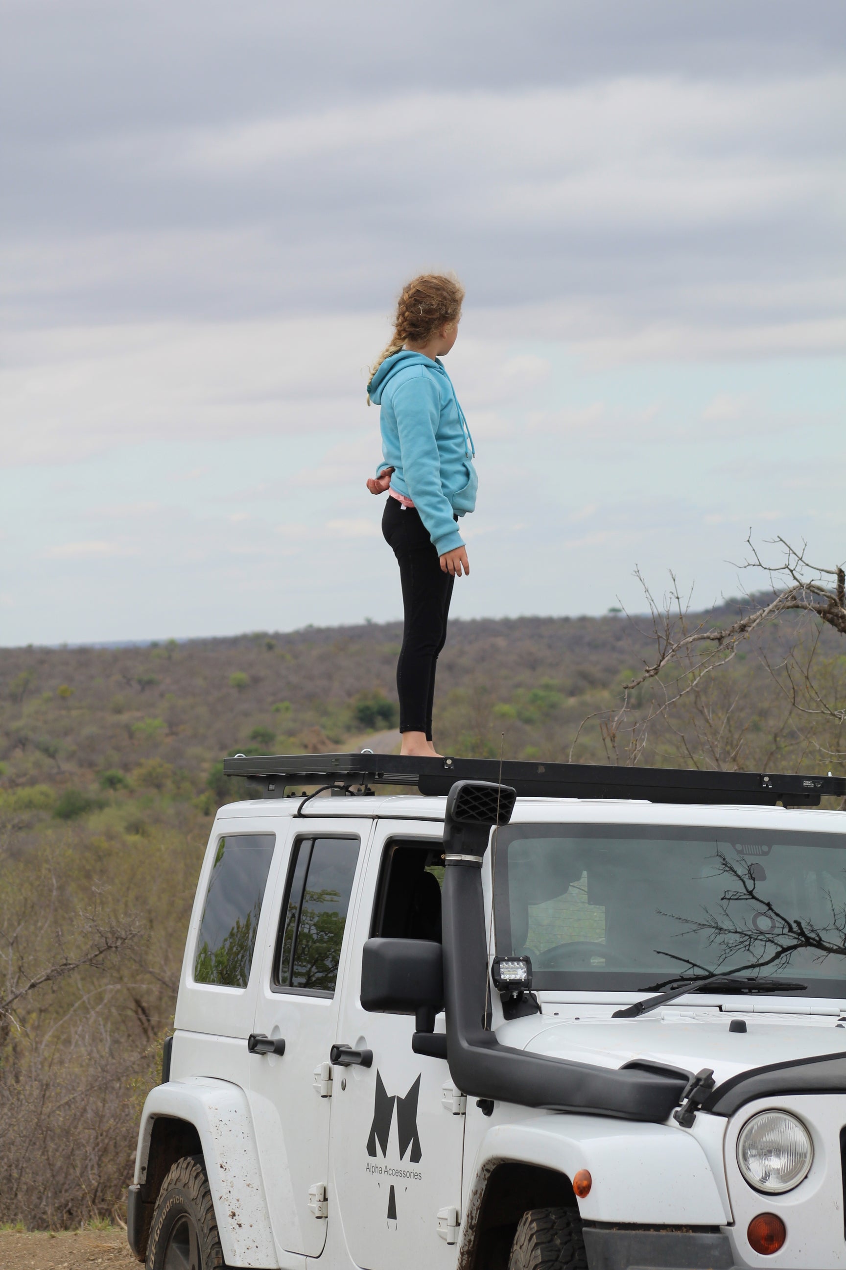 Danyel Kitching standing on the roof rack of a Jeep Wrangler Sahara in Kruger National Park